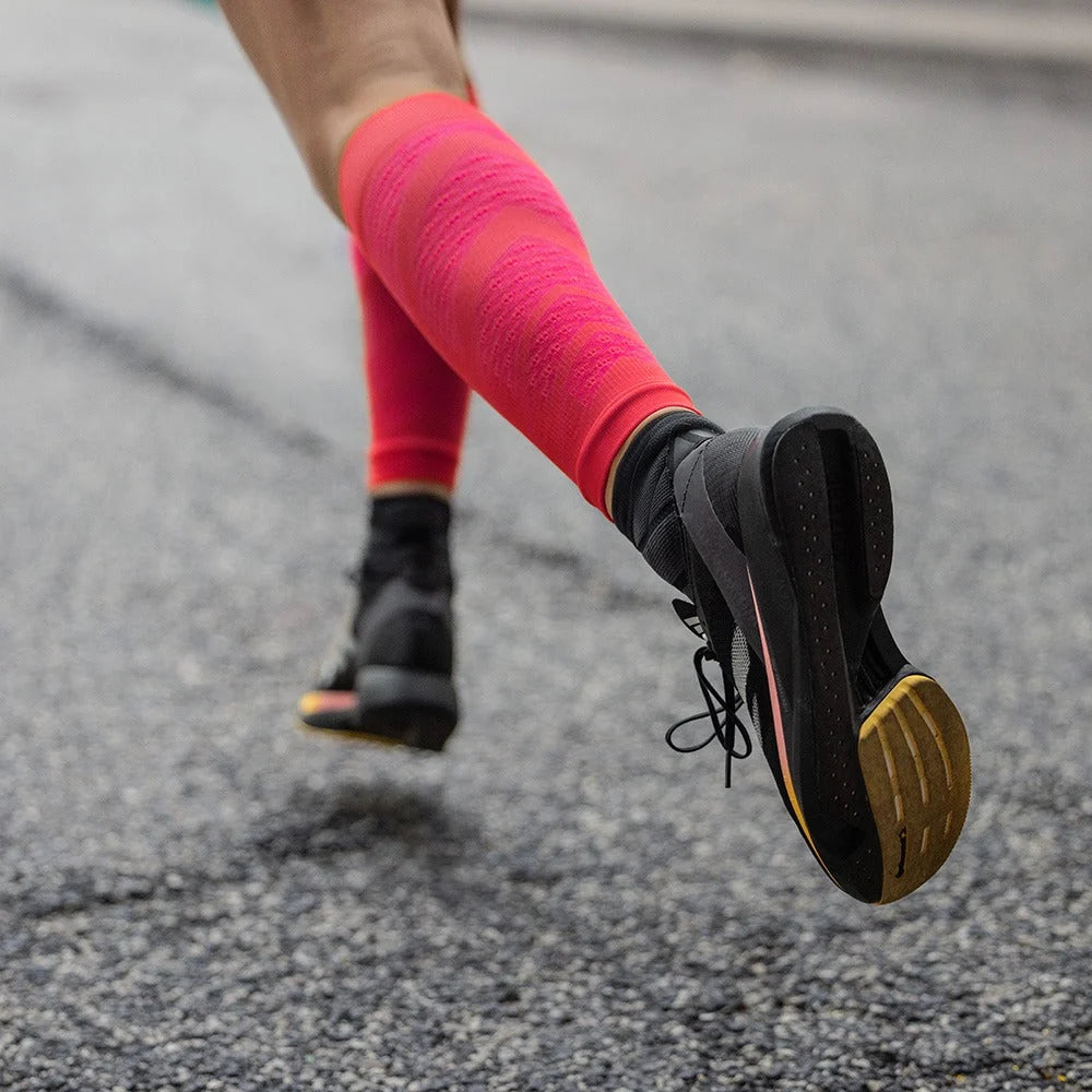 Löpare i korallfärgade Run Performance Compression Sleeves på asfalt