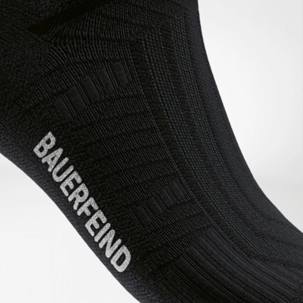 Närbild på fotleden med Bauerfeind-text på den svarta strumpan