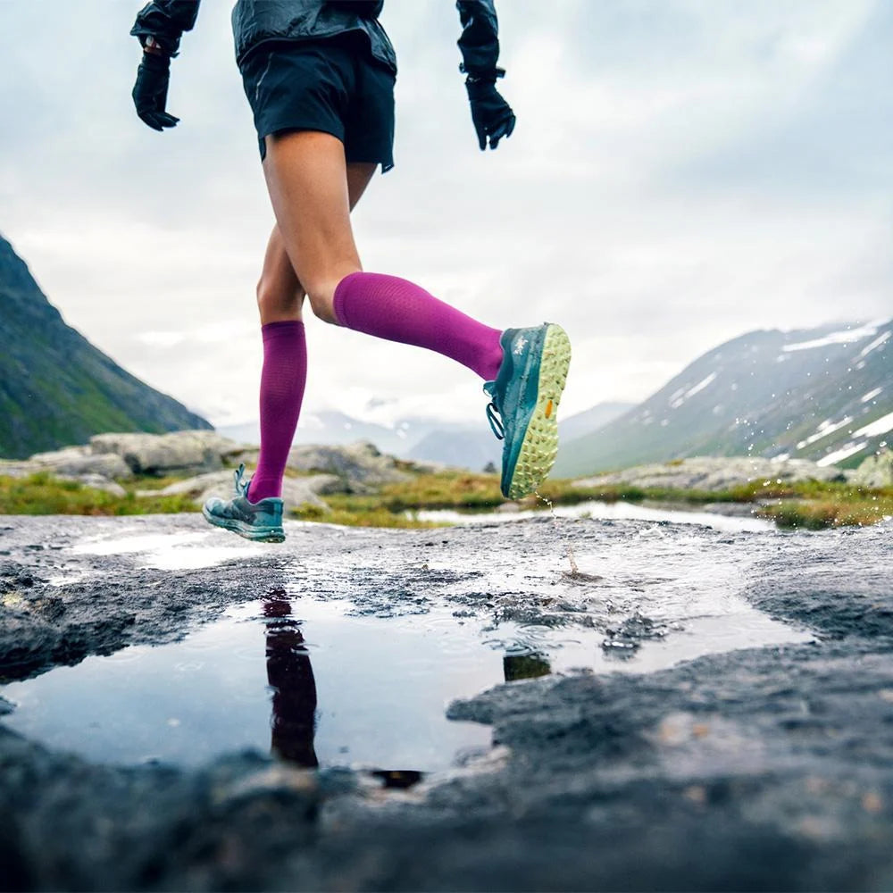 Närbild på löparben med vinröda Run Ultralight-strumpor vid en vattenpöl