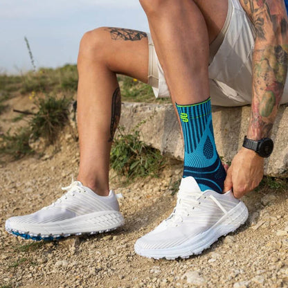 Person sitter på en sten och drar upp Sports Achilles Support över fotleden