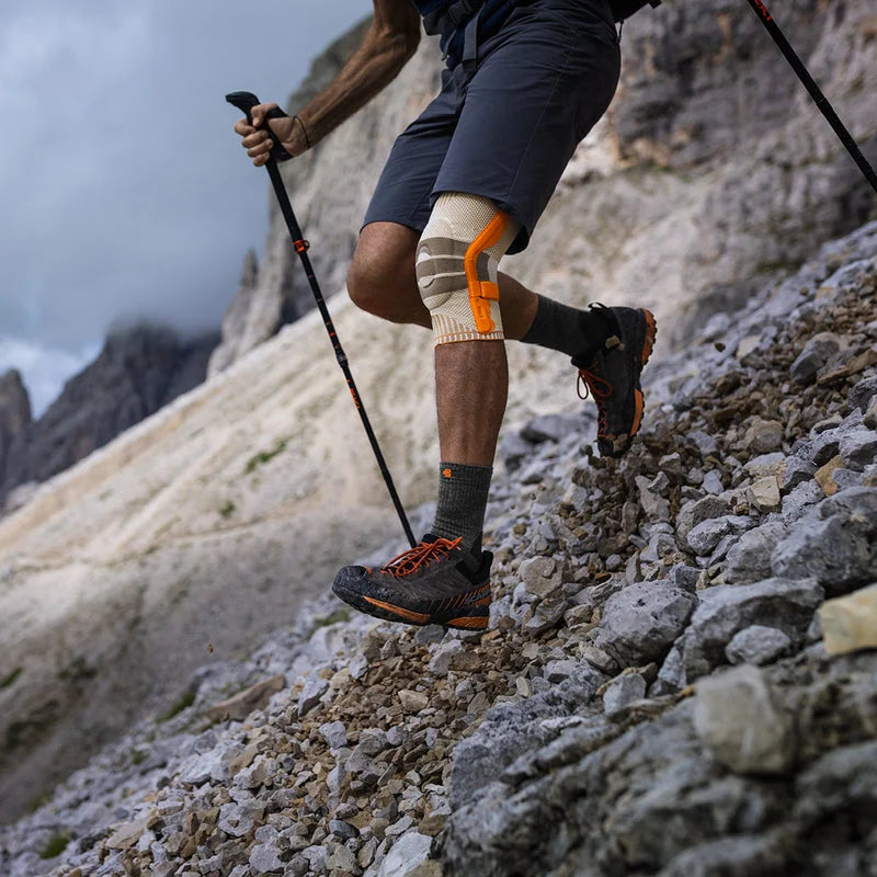 Vandrare med stavar och Sports Outdoor Knee Support på stenig stig