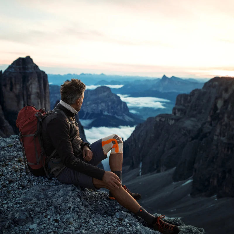 Vandrare med ryggsäck vilar på en bergstopp med knästödet på