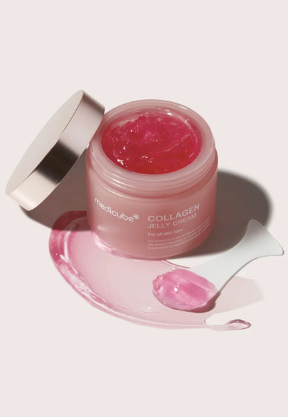 Öppen burk med Medicube Collagen Jelly Cream och rosa gel utsmetad bredvid med spatel på ljus bakgrund.